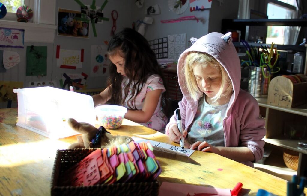 Two girls creating art with markers and stencils on paper